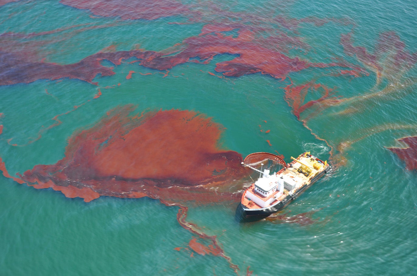 Embarcación rodeada por un derrame petrolero en el océano, contrastando con el agua verde